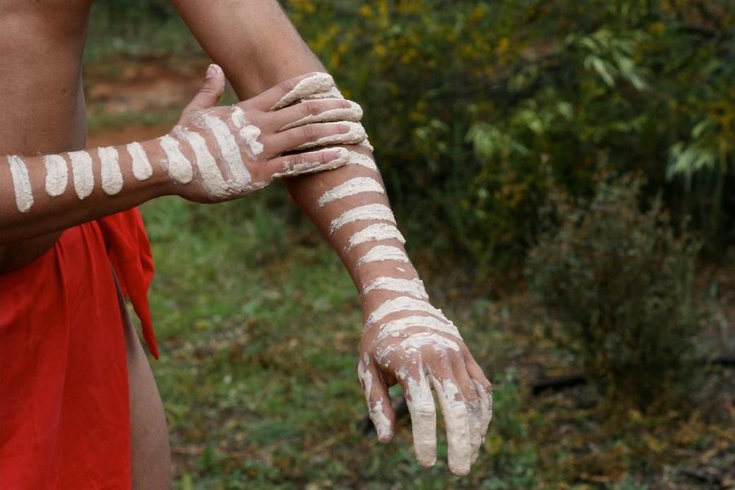 A dancer painting up with white ochre on Country