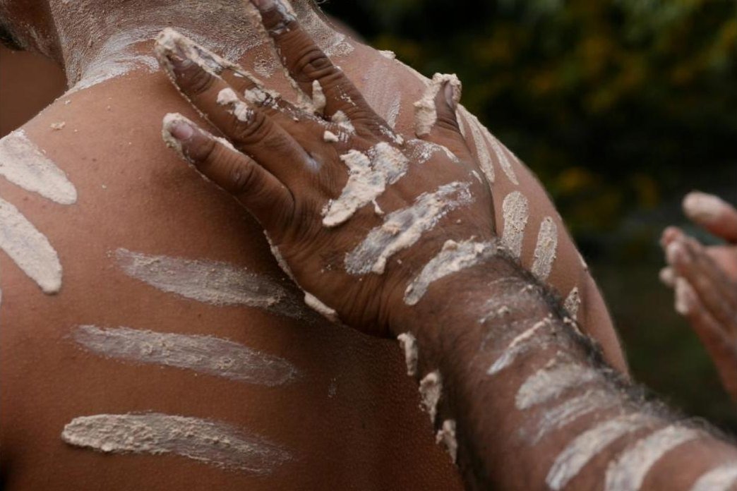 Close-up of a hand painting white ochre onto a dancer's shoulder