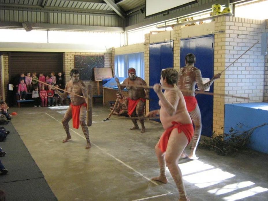 Dancers demonstrating spears in a school hall while students watch