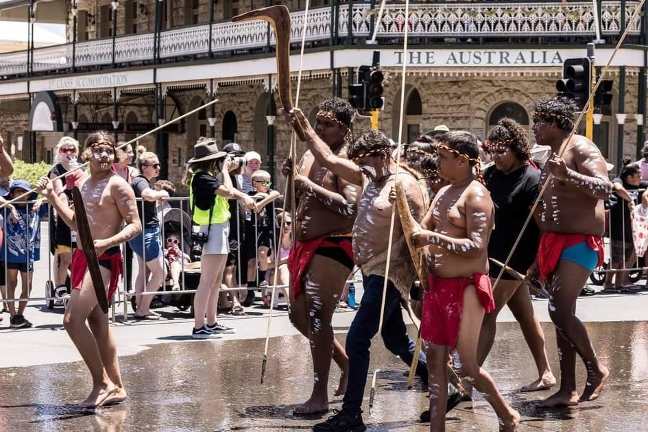 Ngadju dancers in body paint performing down a city street as crowds watch