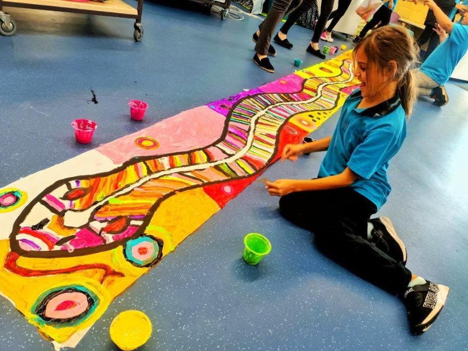 A student painting a long collaborative artwork on the floor