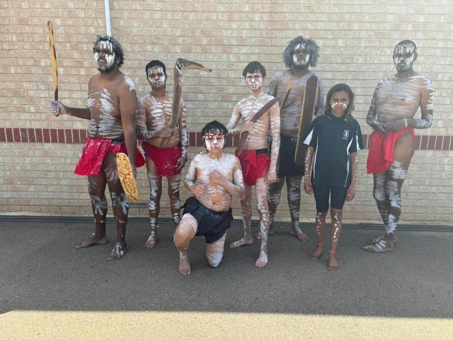 Dancers painted up and holding boomerangs and shields alongside a student